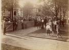 Photograph of crowd in front of Harrison's North Delaware Street home in 1888. Wider view showing crowd in front of Delaware Street home and showing the houses to the north. Brick driveway and sidewalk in foreground.