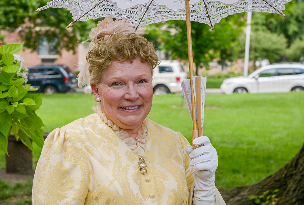Photograph of caroline scott harrison, posed outside of the mansion in a gold dress with white gloves and a white parasol.