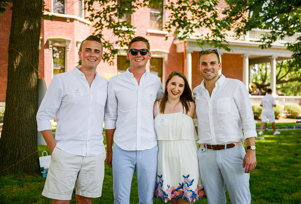 Photograph of people dressed in croquet white clothes, taken in the shade of a large oak tree in the side yard of the presidential home.