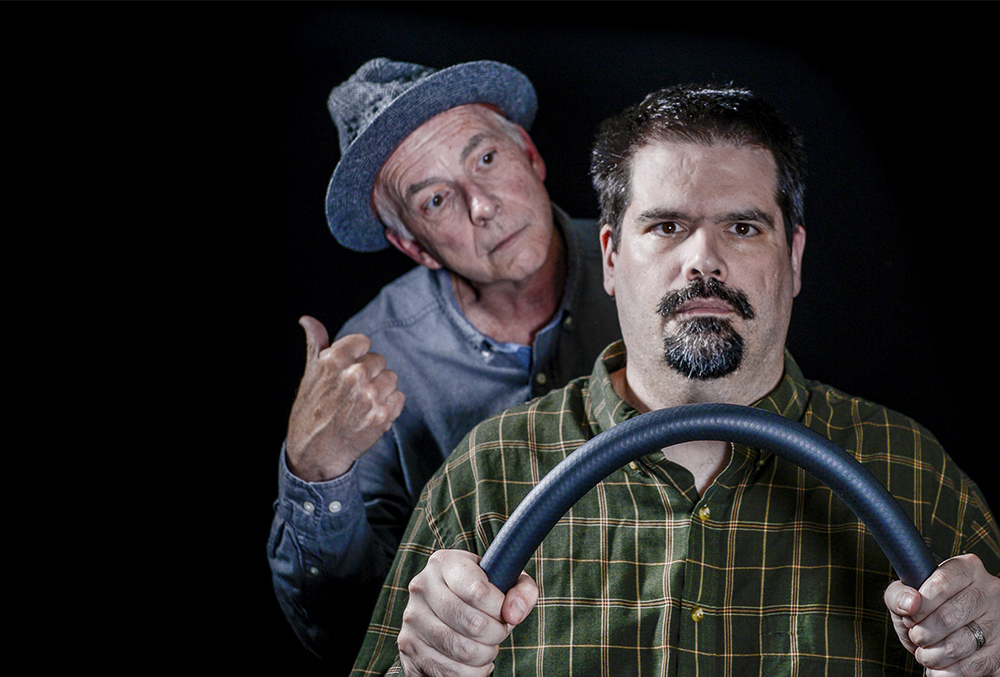Photograph of a hitchhiker looking over the shoulder of a man driving.
