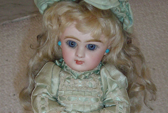 Jumeau doll is 16” tall with original satin dress, leather shoes, earrings, and hat. Her body is molded body with a bisque head. Head marked 