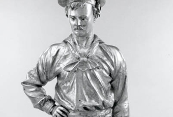 Full figure of a man in sailors uniform with hat. Figure has right hand on hip and left hand at side. Base has inscription 