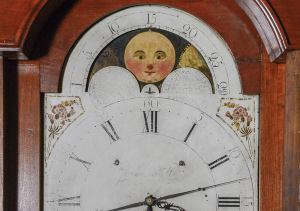 Tall case or grandfather clock made by George Woltz in Hagerstown, Maryland between 1800 and 1812. Clock has moon dial at top and a date dial below the center of the hands, and strikes on the hour. Cherry cabinet with front legs that curve out . There is a spindle on either side of the face. Rounded center at the top with rosette design. Top corners come up to pointed spindles. Clock face is a half circle at top with the dates above the moon dial, Roman numerals and painted floral designs in four corners, and glass door.