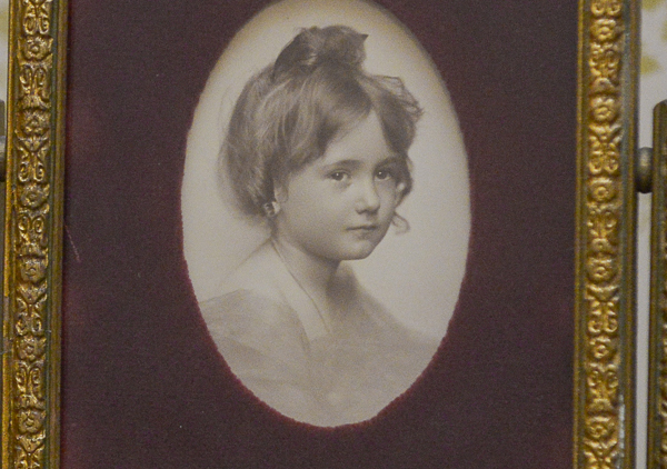 Framed photo of Elizabeth Harrison. Oval photograph window in maroon velvet mat. Gold painted wooden easel type frame with fancy metal base holding wood frame that tilts or swivels up and down.